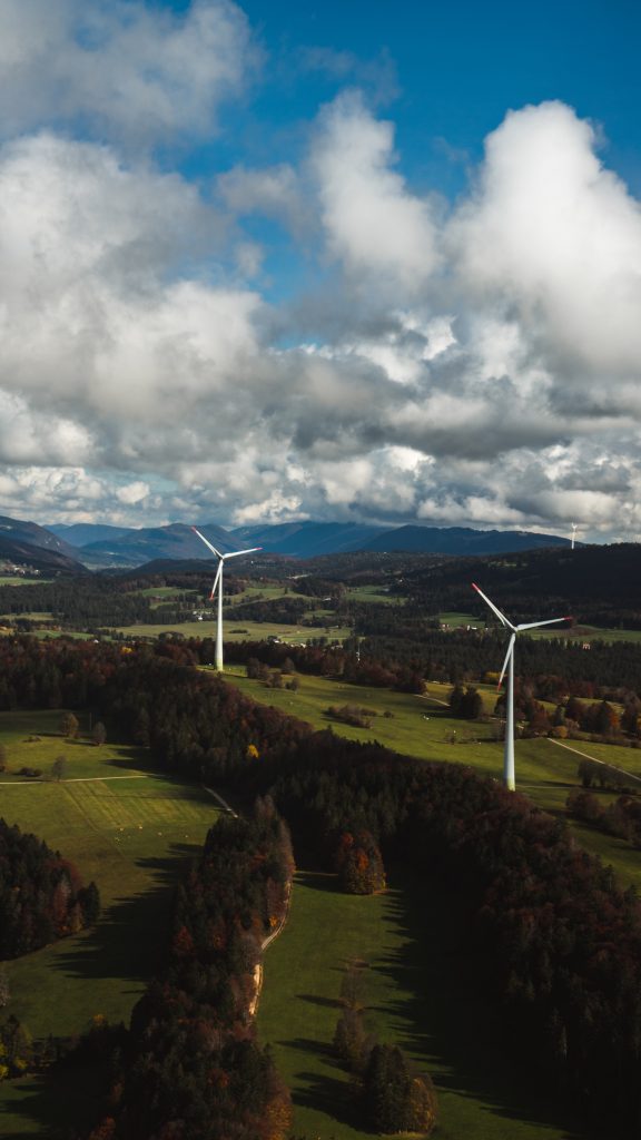 While wind turbines on green grass fields with blue sky and white clouds